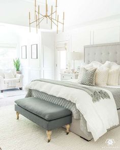 a bedroom with a bed, ottoman and chandelier