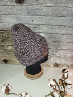 a knitted hat sitting on top of a wooden table next to cotton flowers and leaves