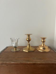 three brass candlesticks sitting on top of a wooden table next to a glass vase