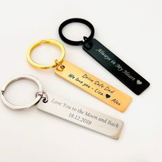 three personalized keychains with names and date engraved on the front, two are gold, one is silver