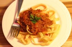 a white plate topped with pasta covered in meat sauce and garnished with parsley