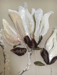 two white flowers with brown leaves on them and some glittery fabric in the middle