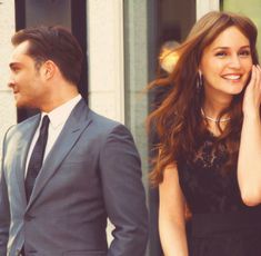 a man and woman walking down the street talking on their cell phones while one holds her hand up to her ear