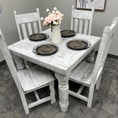 a white table with four chairs around it and a vase filled with flowers on top