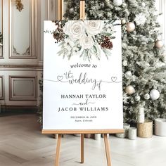 a wedding welcome sign on an easel in front of a christmas tree with pine cones