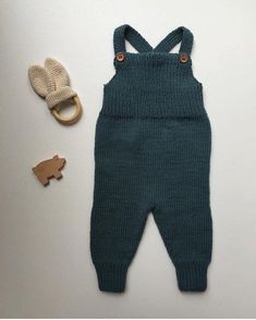 a baby's knitted overall and wooden toy are laying next to it on a white surface