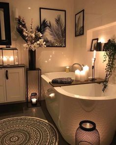 a white bath tub sitting in a bathroom next to candles and pictures on the wall