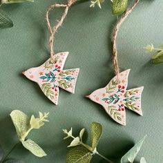 two wooden ornaments hanging from twine with green leaves and red berries on the top