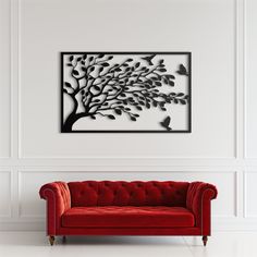 a red couch in front of a white wall with a tree and birds on it