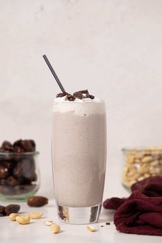 a glass filled with milkshake next to some nuts and chocolate chips on the table