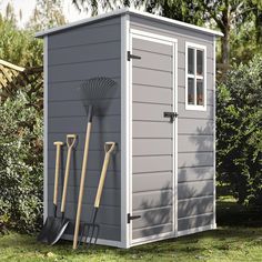 a gray shed with two shovels, a rake and a garden tool next to it