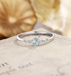 a white gold ring with an aqua blue topazte and diamond accents sits on a piece of paper