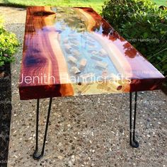 a wooden table sitting on top of a gravel ground next to bushes and trees in the background