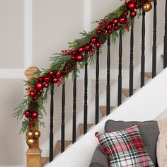 a christmas garland on the banister next to a stair case with red and gold ornaments