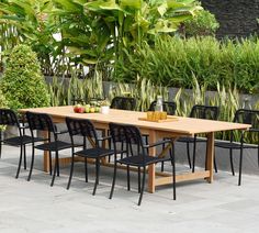 an outdoor dining table with black chairs and plants in the backgroung area