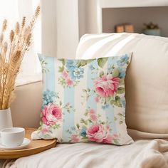 a flowered pillow sitting on top of a white couch next to a cup and saucer