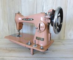 an old pink sewing machine sitting on top of a wooden table next to a wall