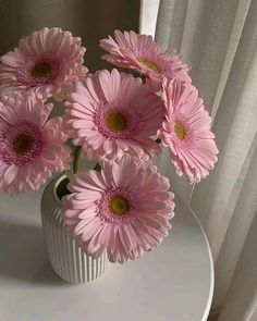 a white vase filled with pink flowers on top of a table