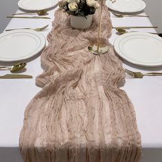 the table is set with white plates, silverware and a vase filled with flowers