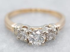 three stone diamond ring on white surface with gold band and two diamonds in the middle