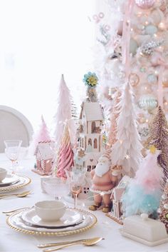 a white table topped with lots of pink and gold christmas decorations next to a tree