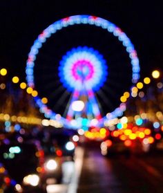 blurry photograph of a ferris wheel at night with lights in the foreground and cars on the street below