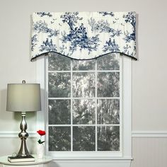 a window with a blue and white flowered valance next to a lamp on a table