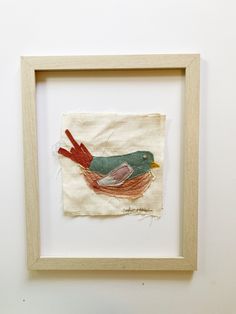 a bird is sitting on top of a piece of fabric in a frame hanging on the wall