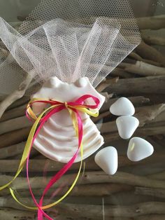 a white bag with yellow and pink ribbons tied around it next to some small pieces of driftwood