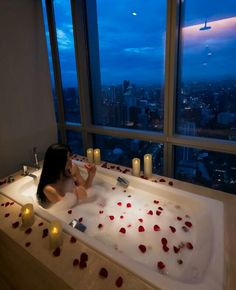 a woman sitting in a bathtub with rose petals on the floor and candles around it