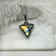 a necklace with a butterfly on it sitting on a marble slab next to feathers and white furnishing