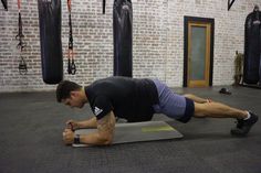 a man doing push ups on a mat in a gym with punching gloves hanging from the wall