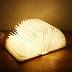 an open book sitting on top of a wooden table next to a light that is turned on