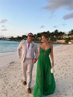 a man and woman in formal wear walking on the beach with their hands in each others'pockets