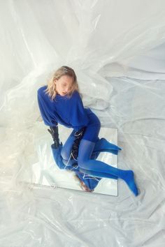 a woman sitting on top of a mirror wearing blue tights and holding her leg in the air