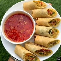 a white plate topped with lots of food next to a bowl of sauce on top of a green field