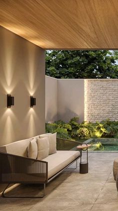 an outdoor living area with couches, tables and lights on the side of the wall