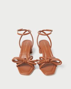 Mid-heel sandal with knotted bow detail in timber brown nappa leather. Features a padded leather footbed with gold stamped logo and an open, squared toe. 2-inch heel.