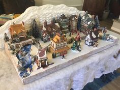 a table topped with lots of small christmas village figurines on top of snow covered ground