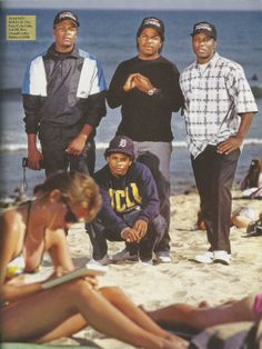 four men standing and sitting on the beach