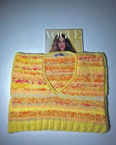 a knitted yellow sweater sitting on top of a white table next to a magazine