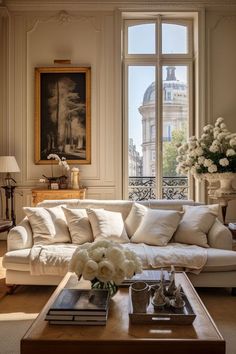 a living room filled with white furniture and flowers on top of a wooden coffee table