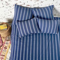 a bed with blue and white striped comforter next to a basket on the floor