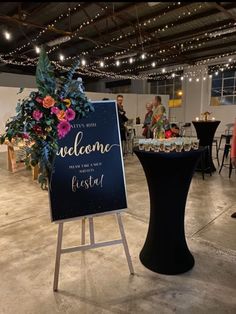 a welcome sign with flowers on it in front of a table and people sitting at tables