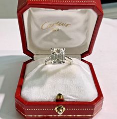 an open red box with a ring in it on top of a white cloth covered table