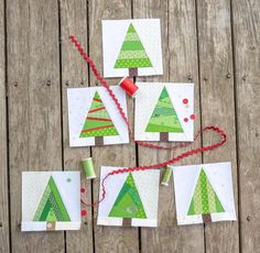 four christmas trees made out of small pieces of paper on a wooden table with red thread