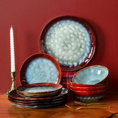 a table topped with plates and candles on top of a wooden table next to a red wall