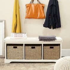 a white bench with baskets underneath it next to a coat rack and two coats hanging on the wall