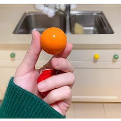 a person holding an orange in their hand near a kitchen sink and stove top oven