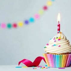 a cupcake with white frosting and sprinkles is sitting in front of a party streamer